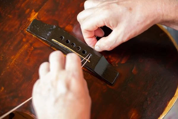 repair-old-guitar-man-inserts-strings-into-holes-tailpiece